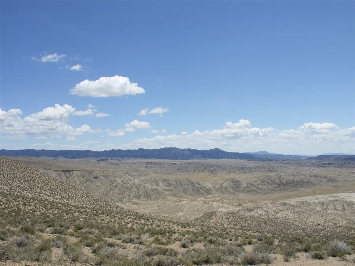 AI-gegenereerde afbeelding: verweerde bleke badlands en een weids leeg plateau bij Galera onder een enorme lucht, in de verte een sierra aan de horizon, geen mensen