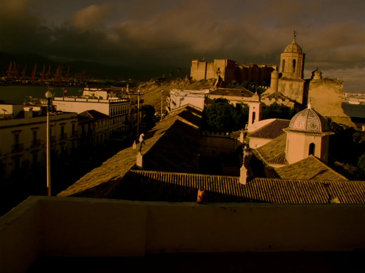 KI-generiertes Bild: die Alcazaba &uuml;ber den ockerfarbenen D&auml;chern von Almer&iacute;a in der tiefen Abendsonne, dahinter gerade noch sichtbare Hafenkr&auml;ne, keine Menschen