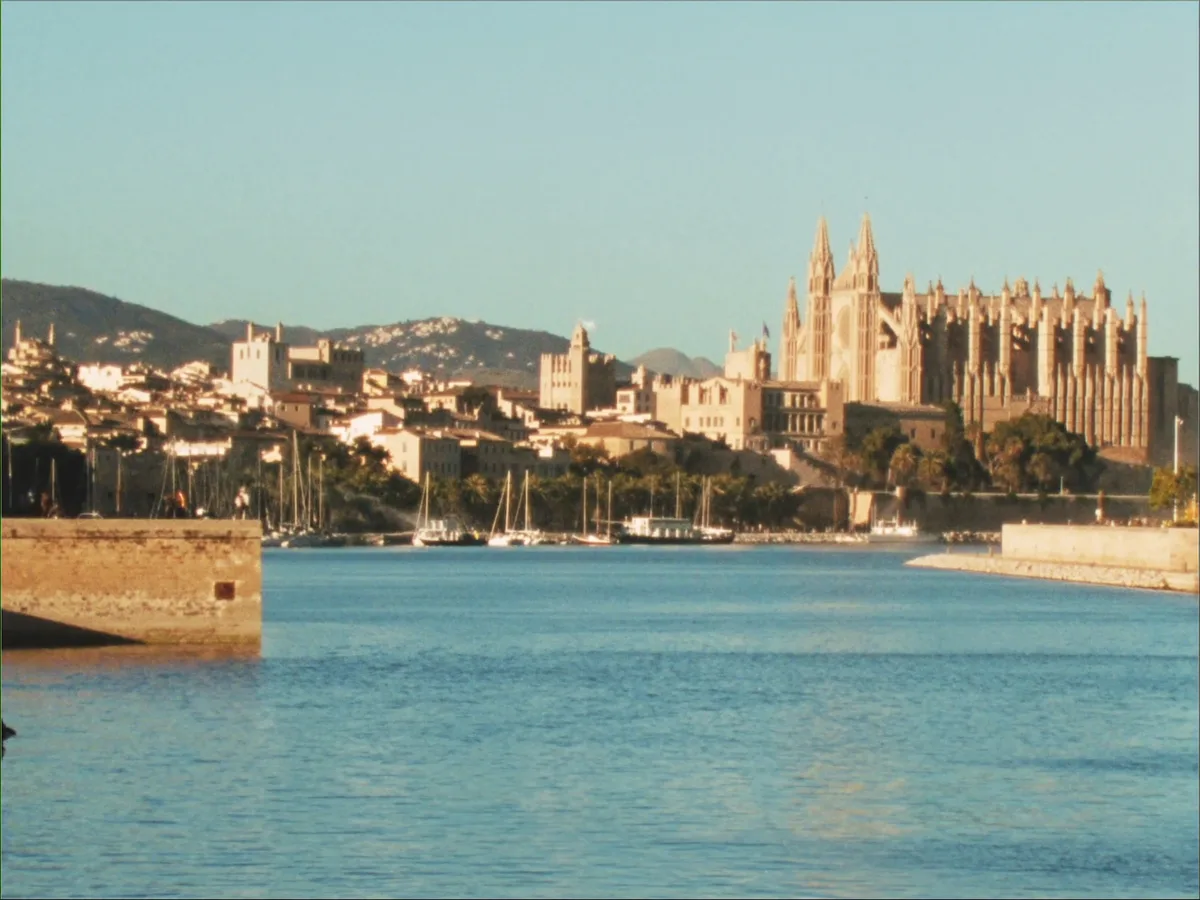 KI-generiertes Bild: die Kathedrale und die Altstadt von Palma &uuml;ber die Bucht hinweg im warmen Morgenlicht, Sandsteinfassaden und die Mauer am Wasser, keine Menschen oder Boote im Vordergrund